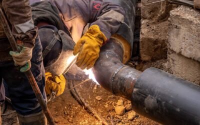 Close-up of a skilled worker welding steel pipes in an industrial setting, showcasing expertise and safety gear.