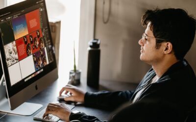A focused graphic designer working on a computer in a modern office setting with creative visuals on the screen.