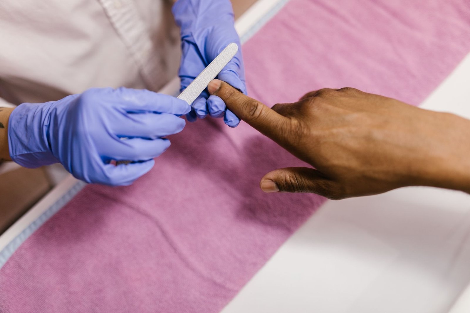Close-up of a manicurist using a nail file on a client's hand during a salon session.
