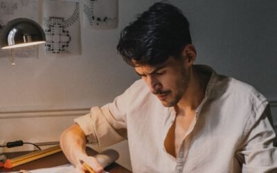 Male architect focused on drawing architectural plans in a well-lit workspace.