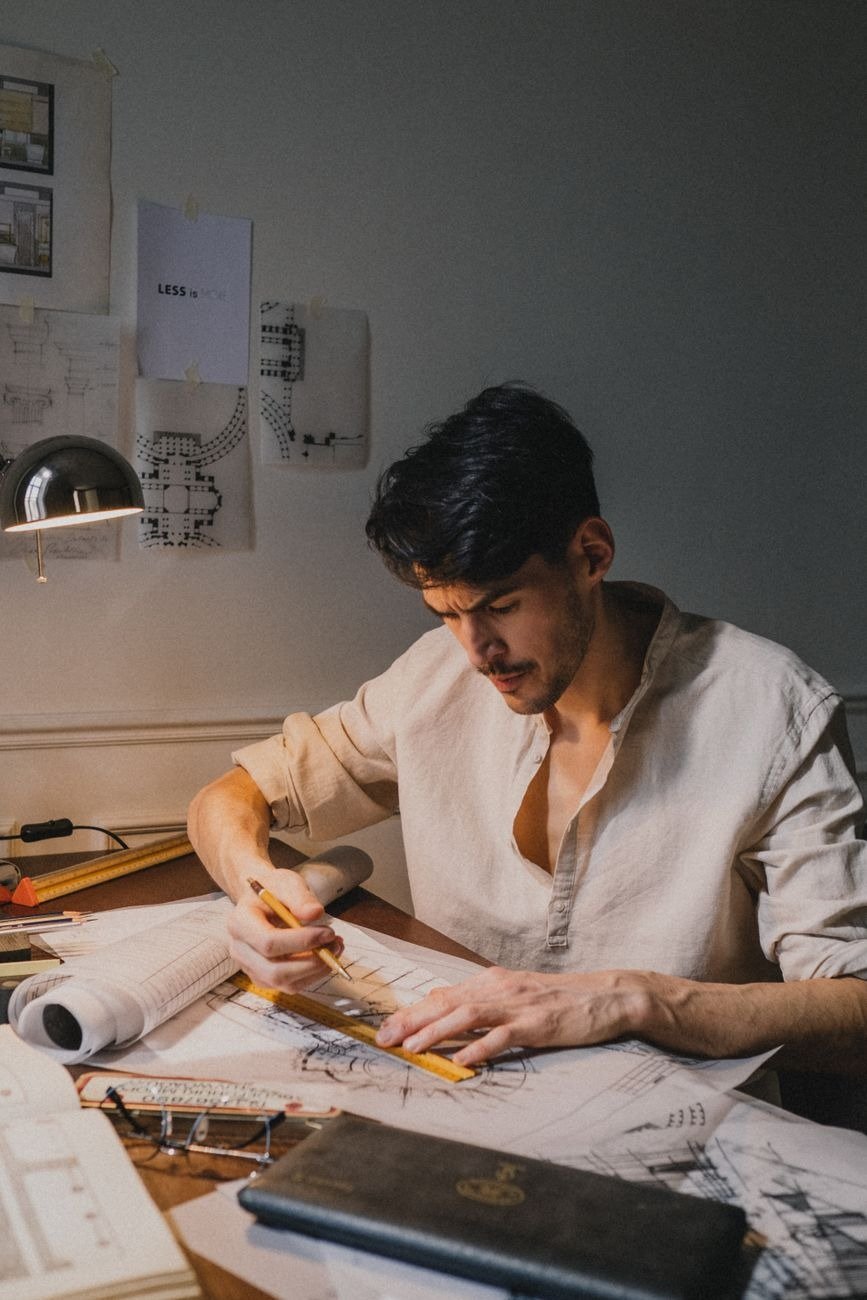Male architect focused on drawing architectural plans in a well-lit workspace.