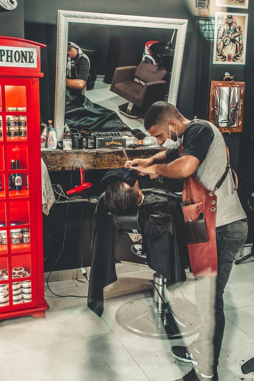 Barber performing a haircut in a stylish barbershop with a mirror reflection.