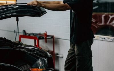 Young mechanic examines a car engine in a dimly lit garage setting, demonstrating auto repair work.