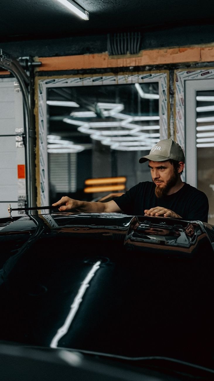 A mechanic carefully working on a black car in a modern auto repair garage.