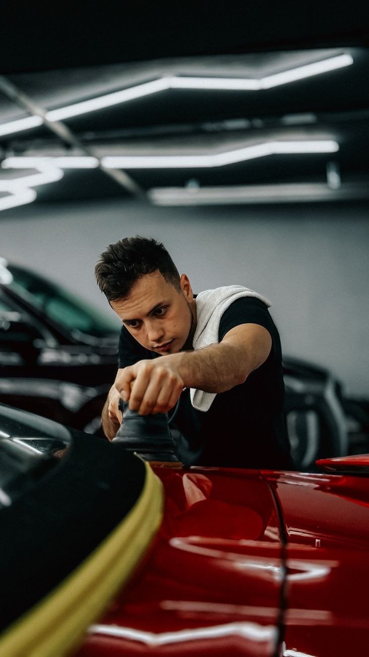 Focused man polishing a red car in a modern, well-lit workshop.
