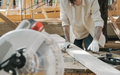 A carpenter uses a circular saw on a wood plank in an outdoor construction setting.