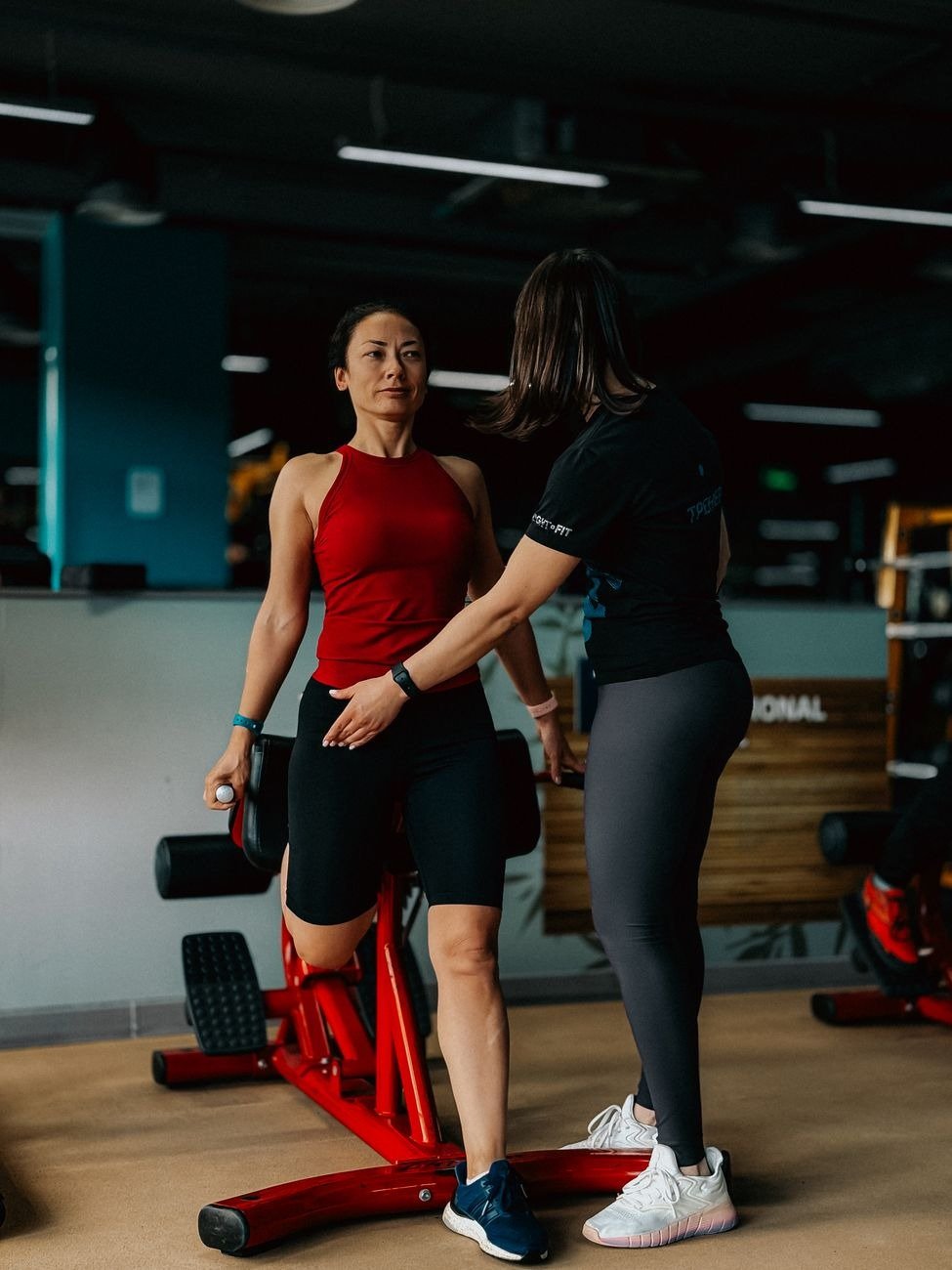 A personal trainer assisting a client with fitness exercises in a modern gym setting.