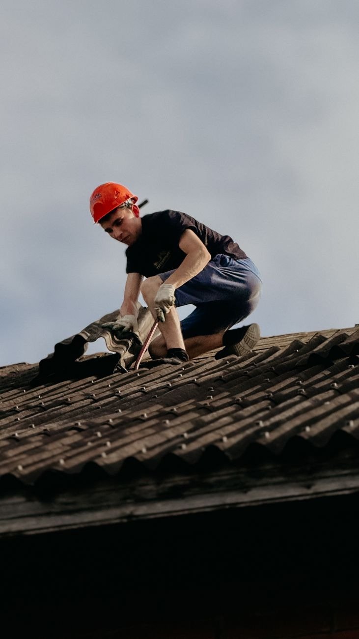 A construction worker with a safety helmet is repairing a roof outdoors during the day.