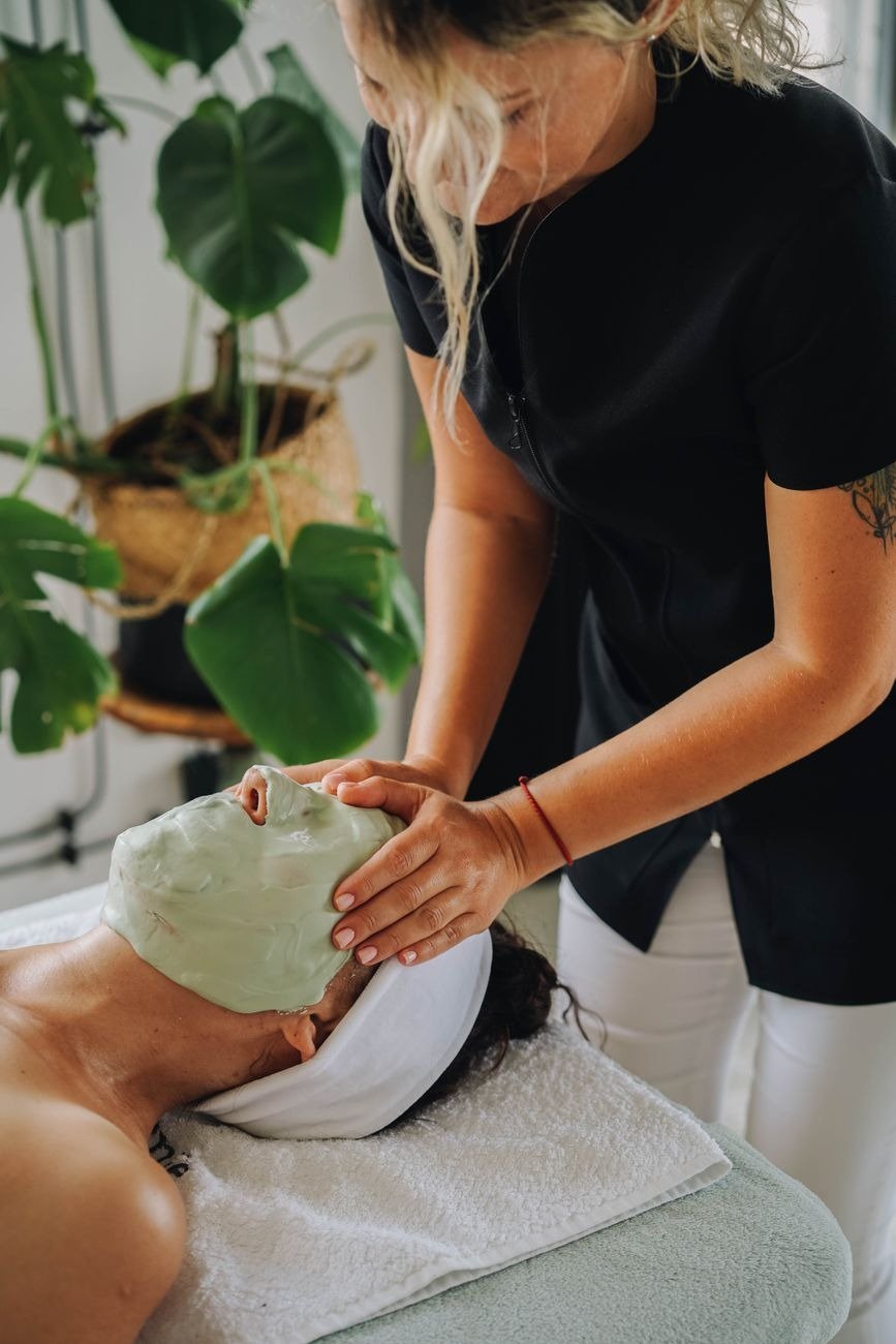 Woman relaxing with a rejuvenating face massage and green cosmetic mask in a tranquil spa setting.