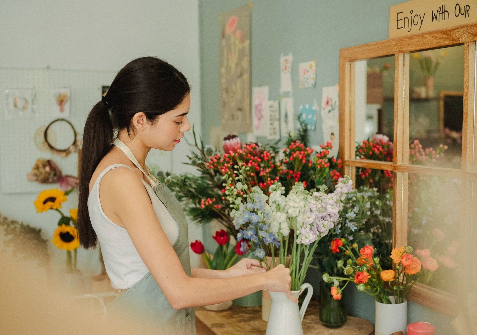 Side view of serious female florist arranging fresh flowers in vase while working in florist studio