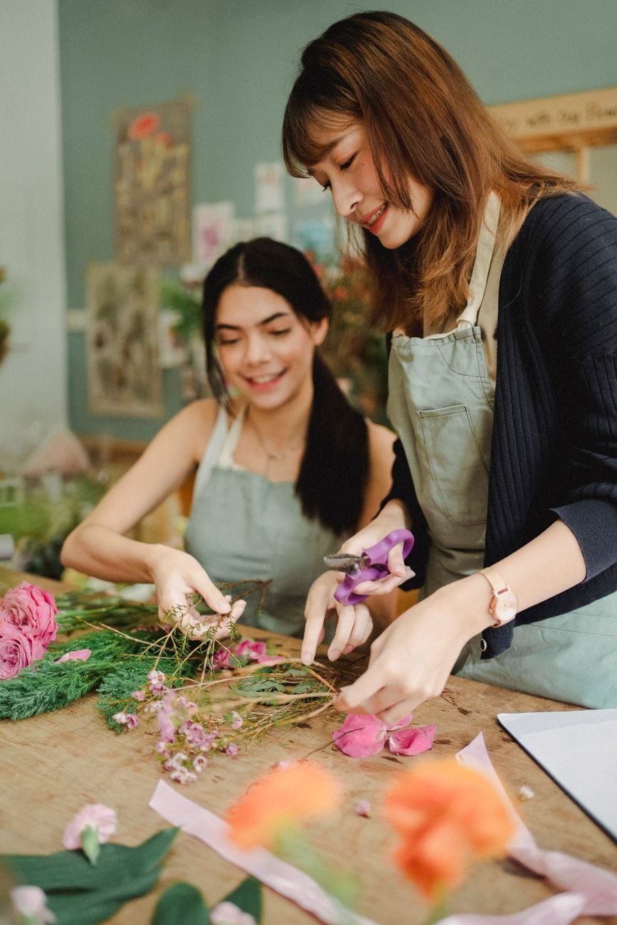 Young smiling multiracial female floral designers creating flower compositions while working in shop together