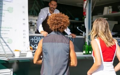 Hospitable ethnic man in apron standing at counter and helping diverse customers with choice while working in food truck