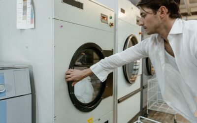 An adult man wearing a white shirt using a washing machine in a modern laundry facility.