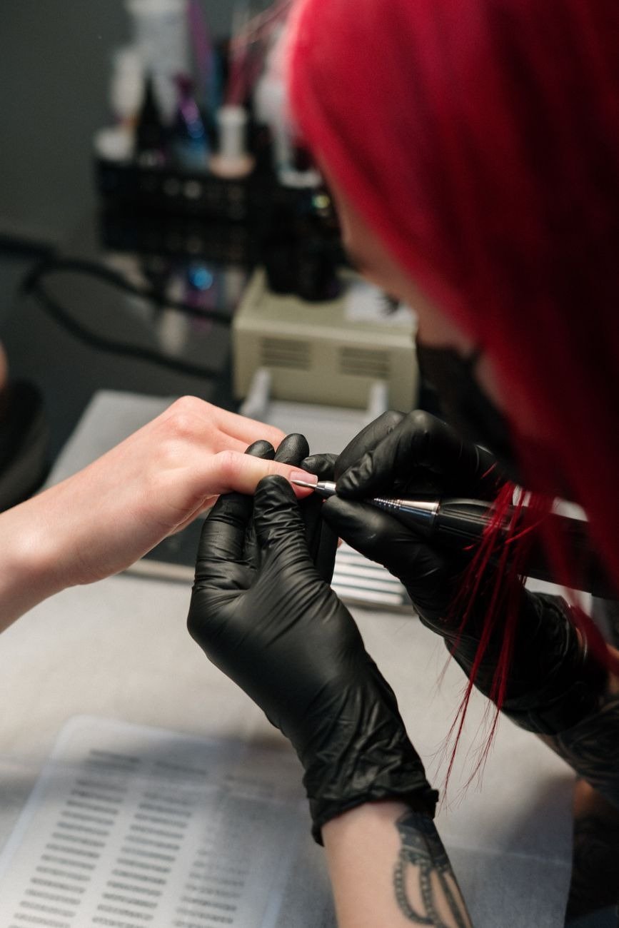 Nail technician with red hair performing a manicure wearing black gloves.