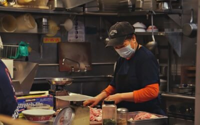 A woman in a kitchen wears a face mask while cutting meat, showcasing food preparation safety.