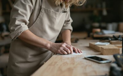 Une menuisière ponce une planche, un téléphone posé face contre l'établi sonne à côté