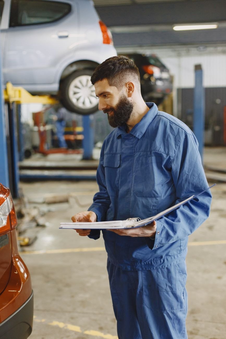 Mechanic in blue coverall examining documents in a bustling auto workshop.